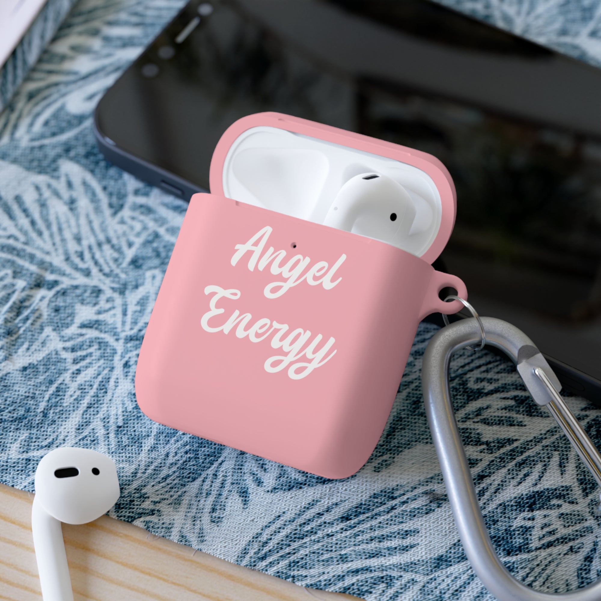 Pink AirPods case with 'Angel Energy' text on a blue patterned surface.